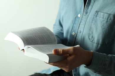 Man reading Holy Bible in English language on light background, closeup