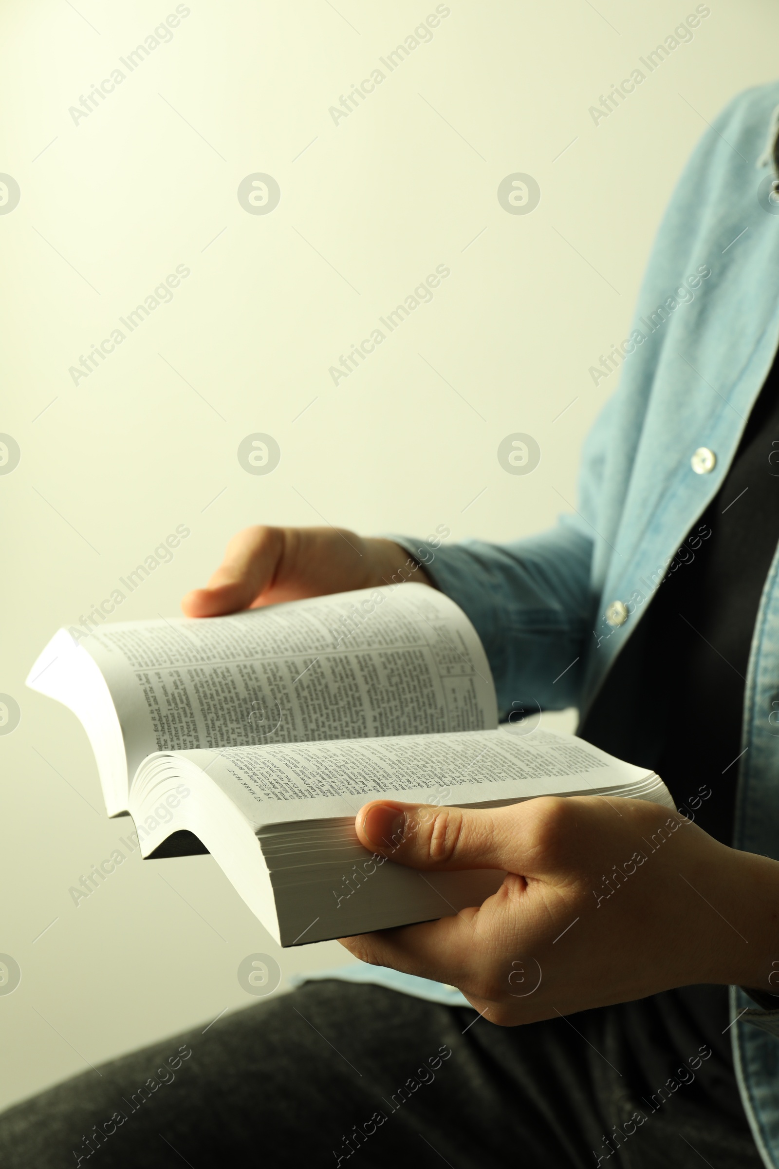 Photo of Man reading Holy Bible in English language on light background, closeup