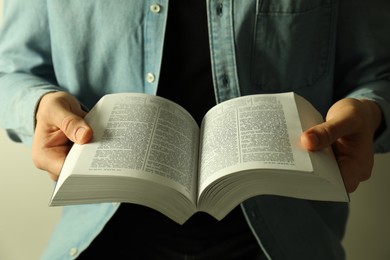 Photo of Man reading Holy Bible in English language on light background, closeup