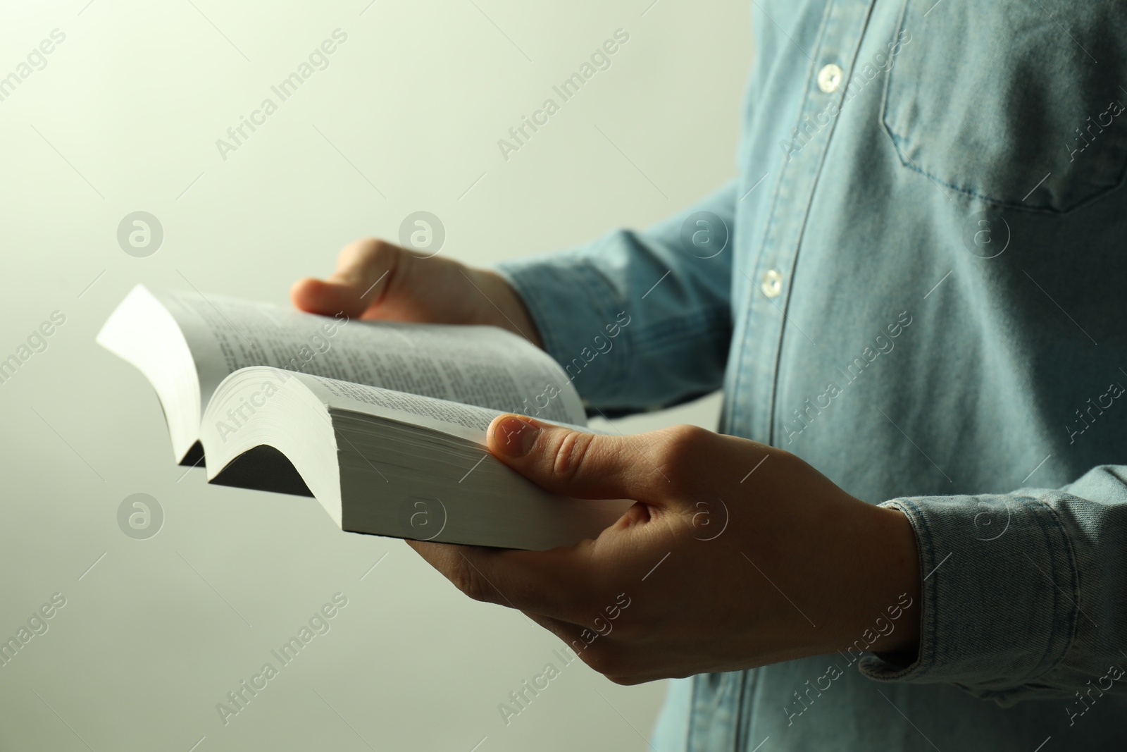 Photo of Man reading Holy Bible in English language on light background, closeup