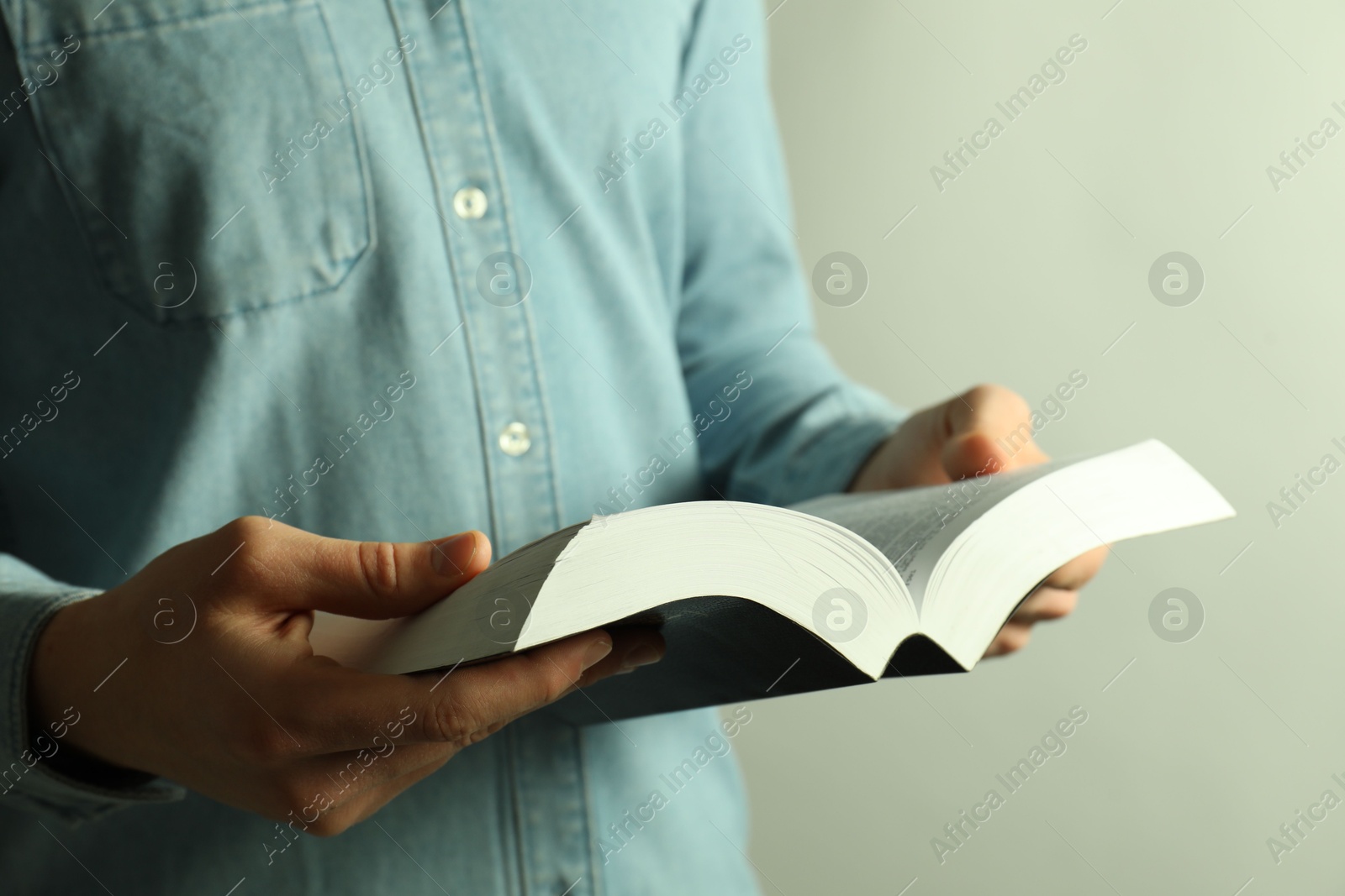 Photo of Man reading Holy Bible in English language on light background, closeup