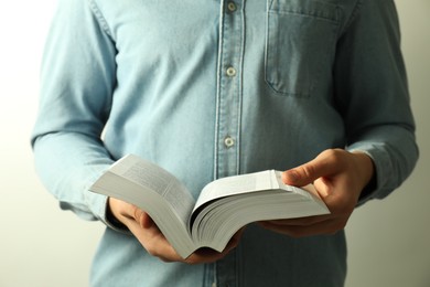 Man reading Holy Bible in English language on light background, closeup