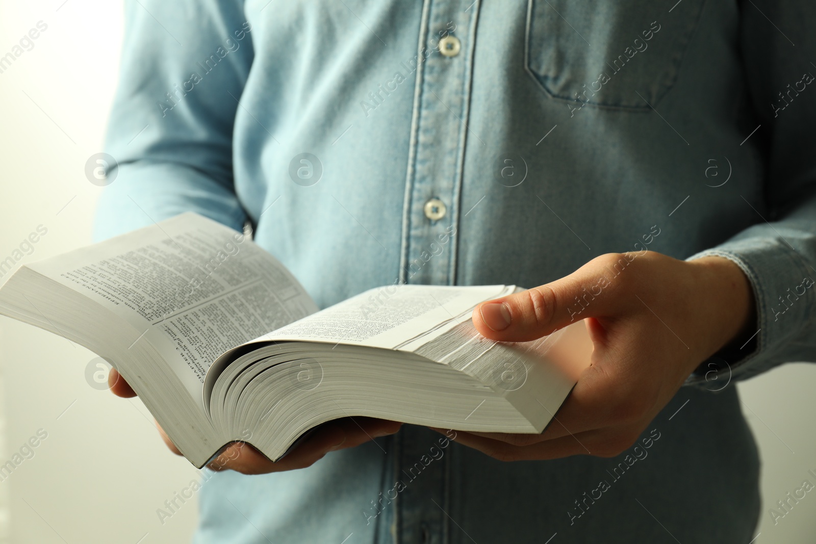 Photo of Man reading Holy Bible in English language on light background, closeup