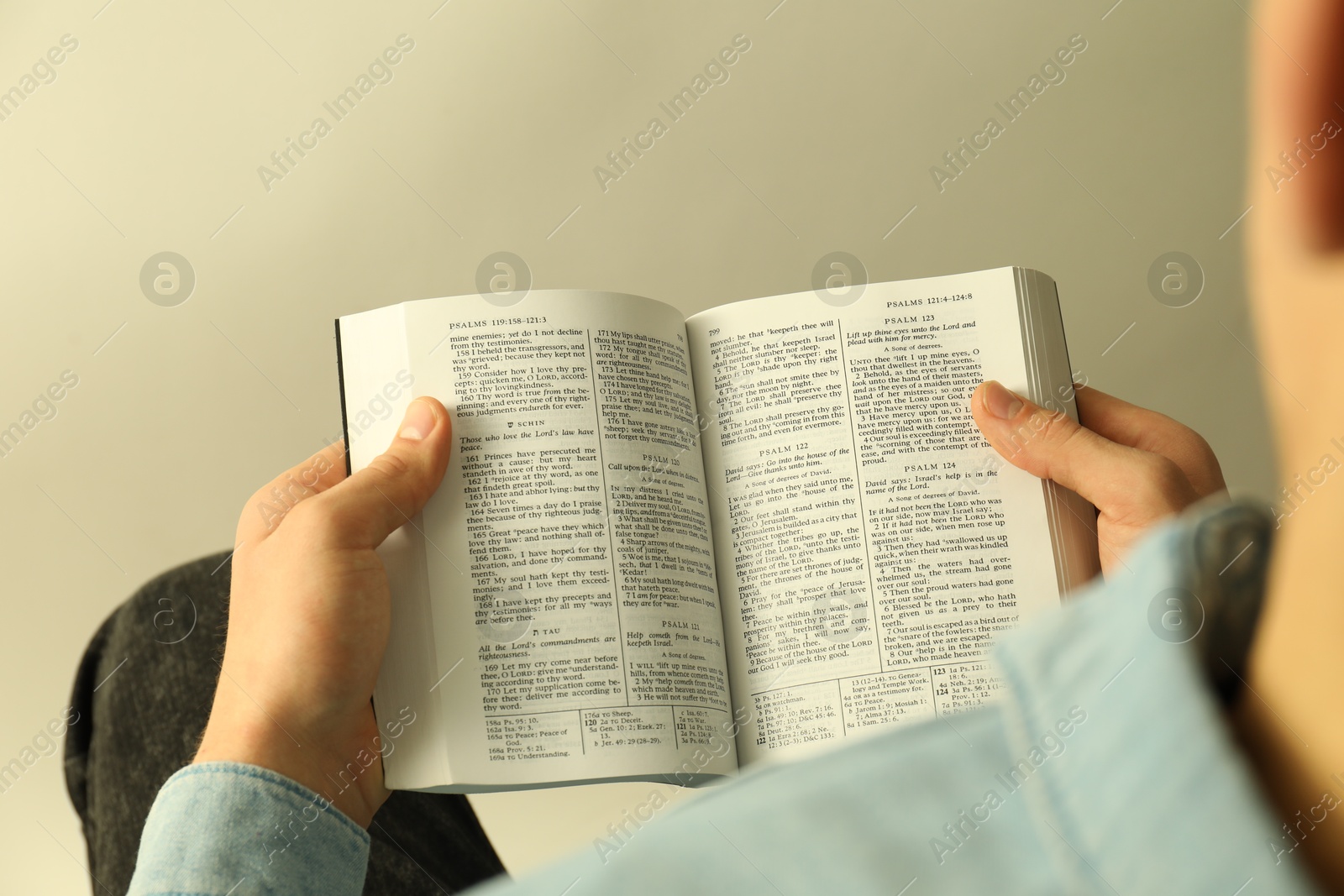 Photo of Man reading Holy Bible in English language on light background, closeup