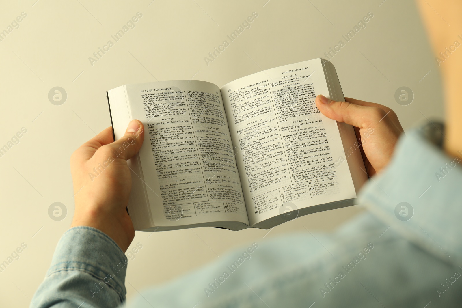 Photo of Man reading Holy Bible in English language on light background, closeup