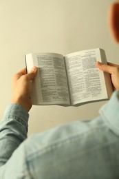 Photo of Man reading Holy Bible in English language on light background, closeup