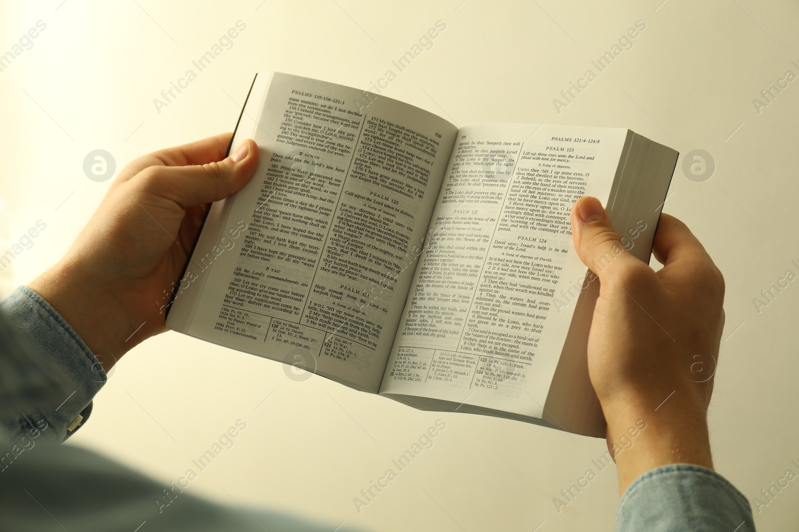 Photo of Man reading Holy Bible in English language on light background, closeup