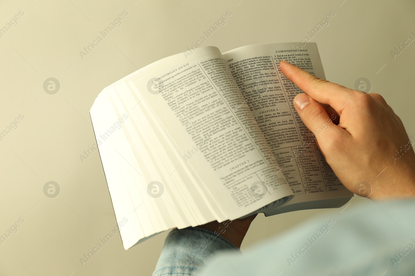 Photo of Man reading Holy Bible in English language on light background, closeup