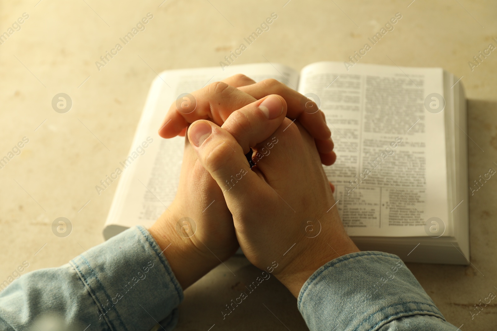 Photo of Man with open Holy Bible praying at grey table, closeup