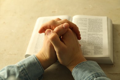 Photo of Man with open Holy Bible praying at grey table, closeup