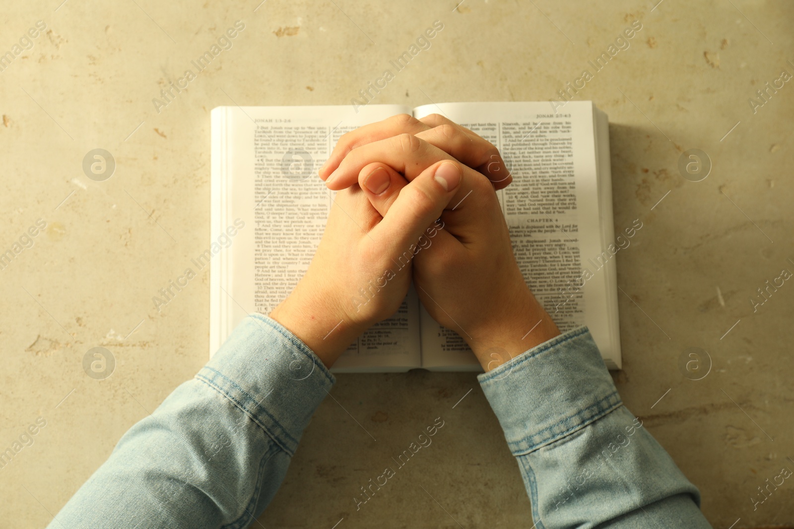 Photo of Man with open Holy Bible praying at grey table, top view