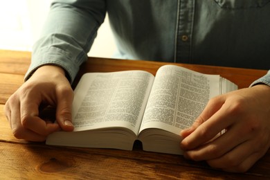 Man reading Holy Bible in English language at wooden table, closeup