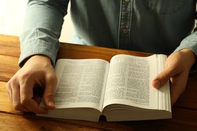 Photo of Man reading Holy Bible in English language at wooden table, closeup