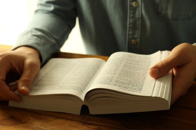 Photo of Man reading Holy Bible in English language at wooden table, closeup