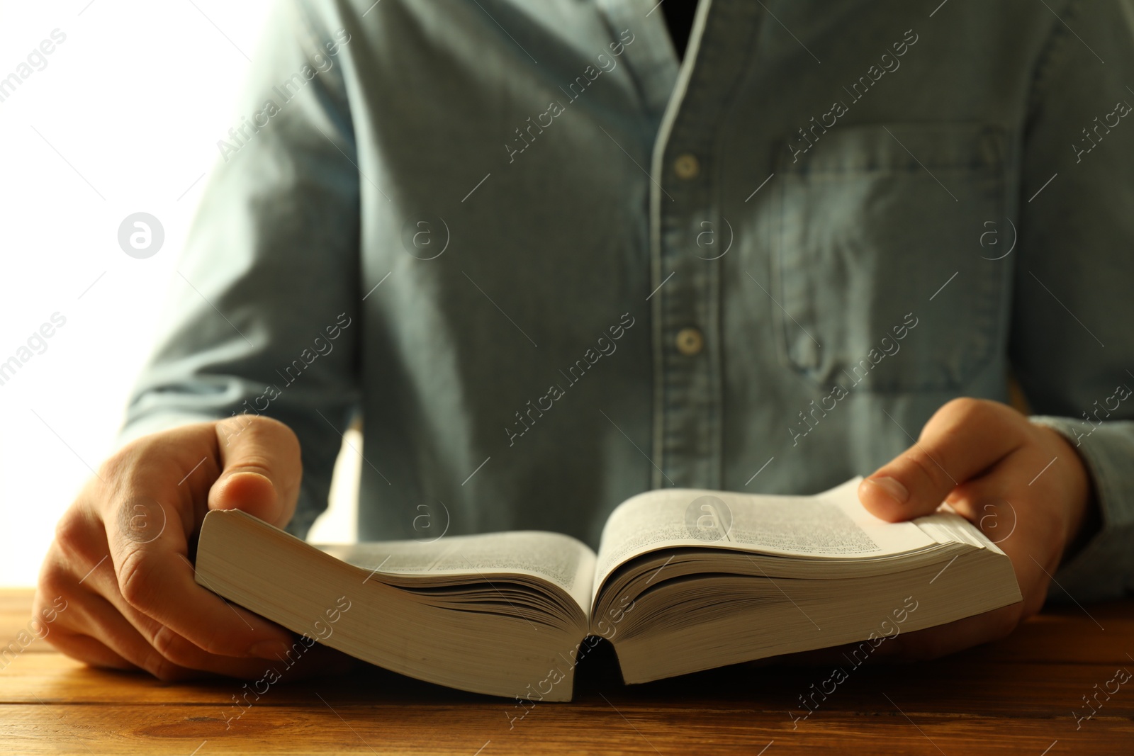 Photo of Man reading Holy Bible in English language at wooden table, closeup