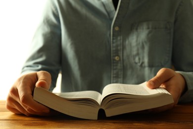 Man reading Holy Bible in English language at wooden table, closeup