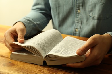 Photo of Man reading Holy Bible in English language at wooden table, closeup