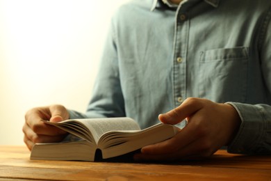 Photo of Man reading Holy Bible in English language at wooden table, closeup