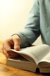 Photo of Man reading Holy Bible in English language at wooden table, closeup