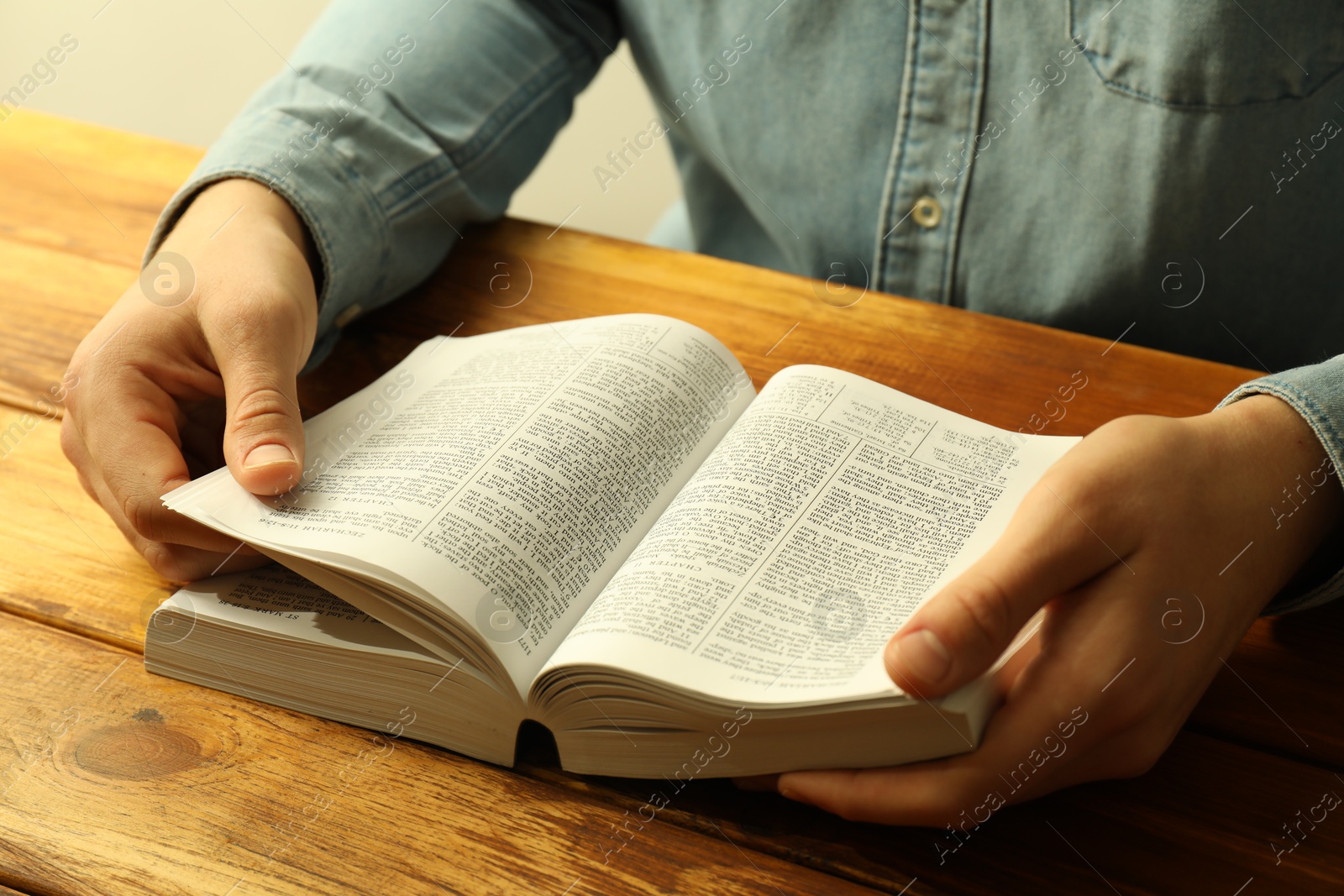 Photo of Man reading Holy Bible in English language at wooden table, closeup