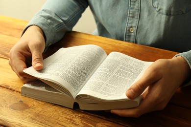 Man reading Holy Bible in English language at wooden table, closeup