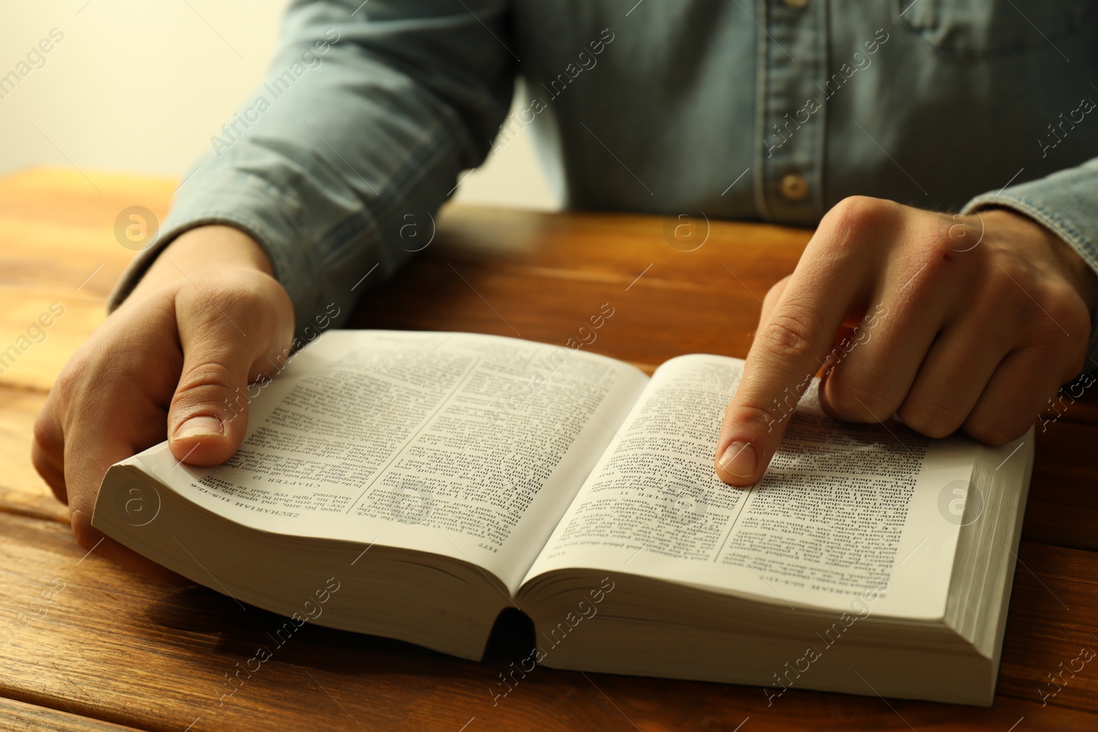 Photo of Man reading Holy Bible in English language at wooden table, closeup