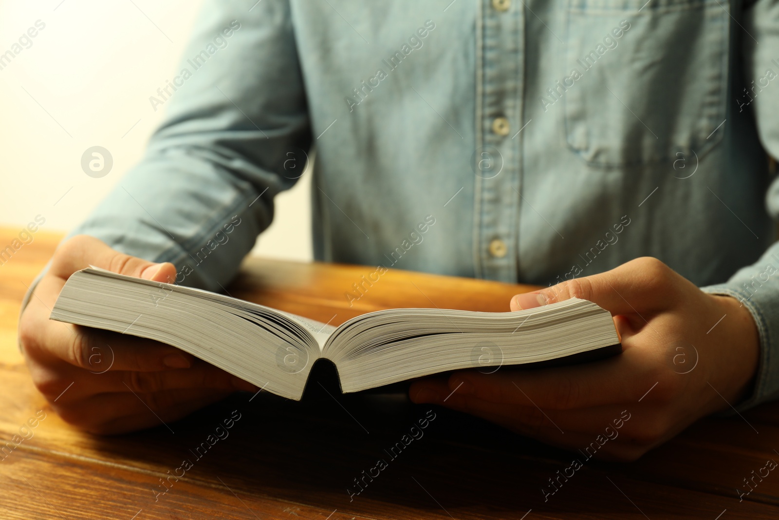 Photo of Man reading Holy Bible at wooden table, closeup