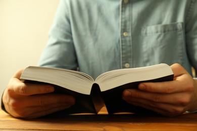 Photo of Man reading Holy Bible at wooden table, closeup