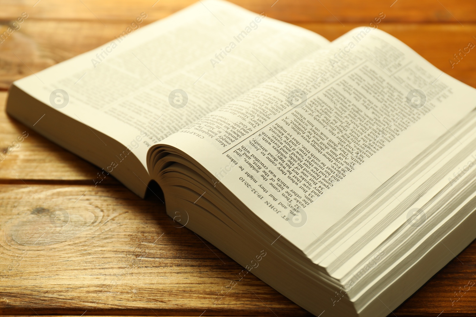 Photo of Open Holy Bible in English language on wooden table, closeup