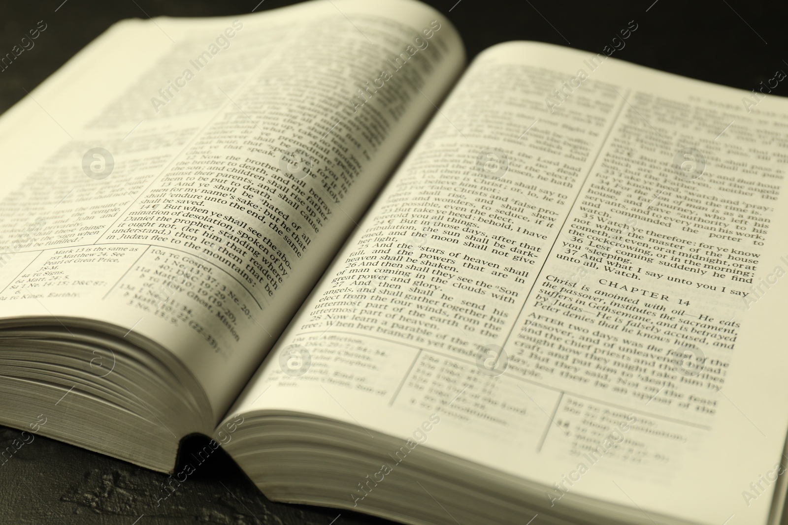 Photo of Open Holy Bible in English language on black table, closeup