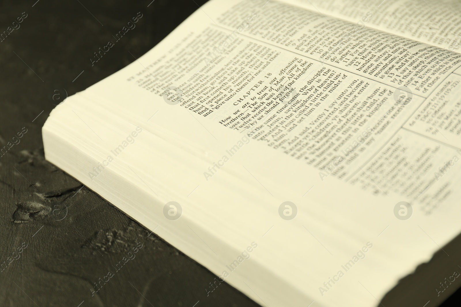 Photo of Open Holy Bible in English language on black table, closeup