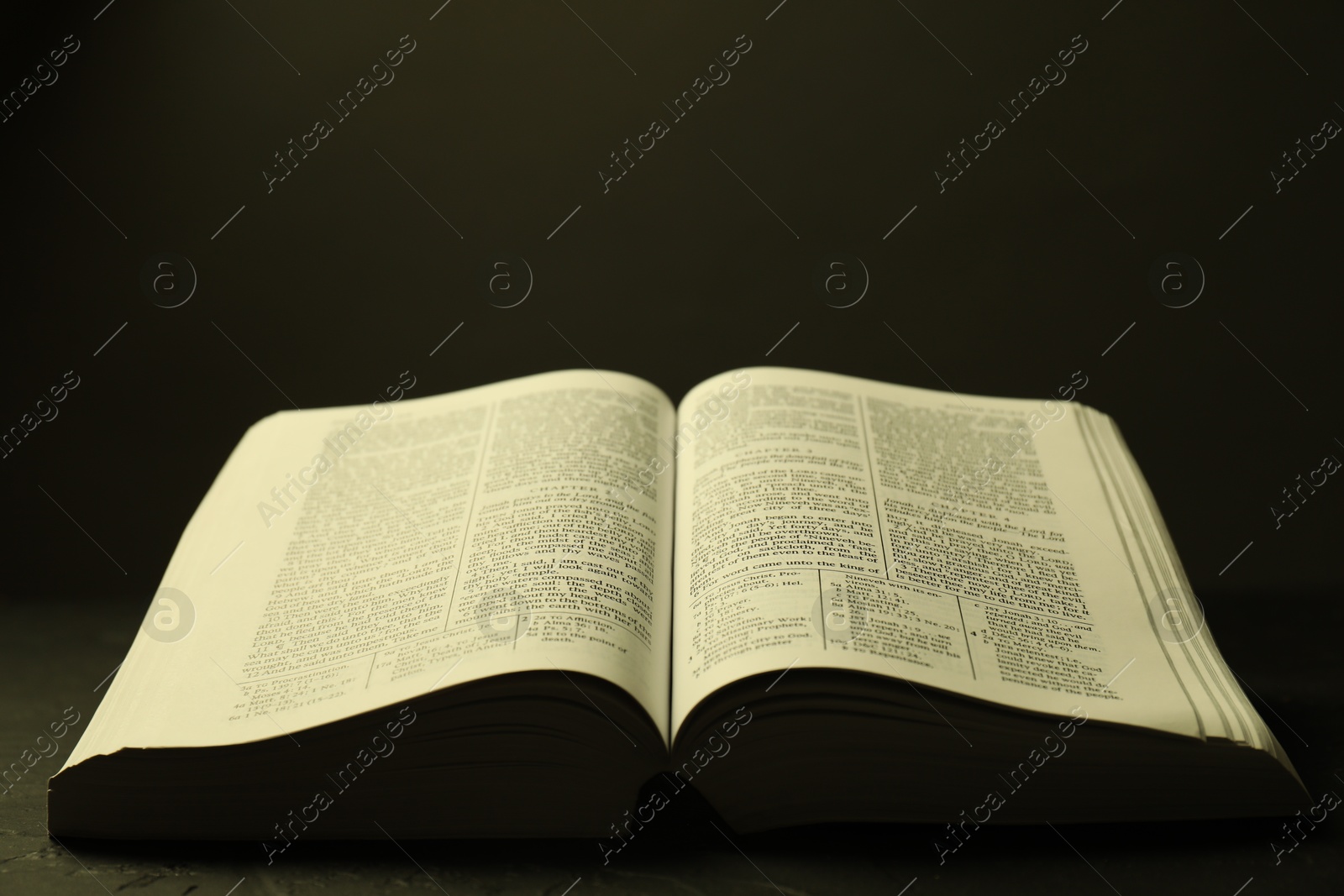 Photo of Open Holy Bible in English language on black table, closeup