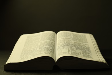 Photo of Open Holy Bible in English language on black table, closeup