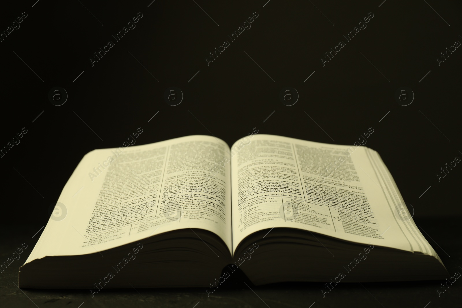 Photo of Open Holy Bible in English language on black table, closeup