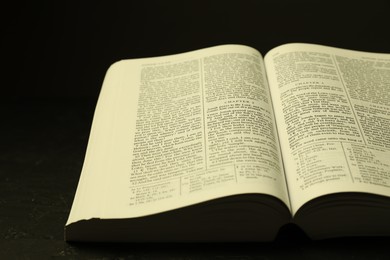 Photo of Open Holy Bible in English language on black table, closeup