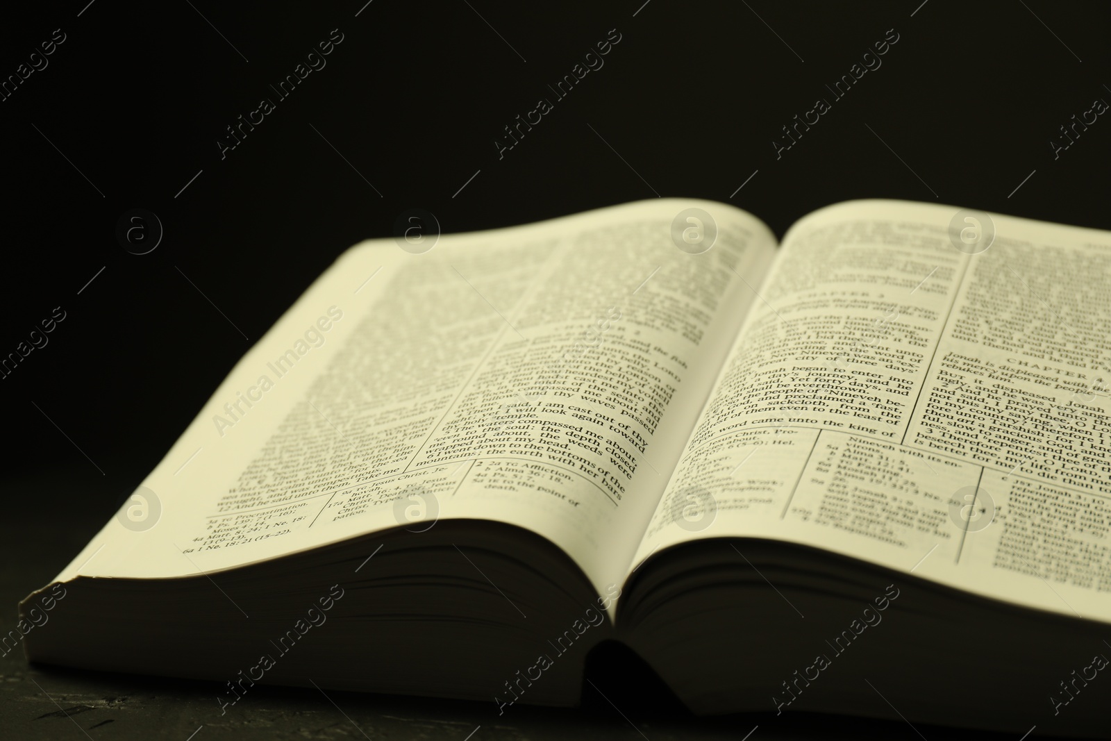 Photo of Open Holy Bible in English language on black table, closeup