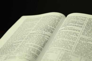 Photo of Open Holy Bible in English language on black background, closeup