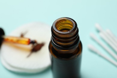 Photo of Bottle of topical iodine, cotton pads and swabs on light blue background, selective focus