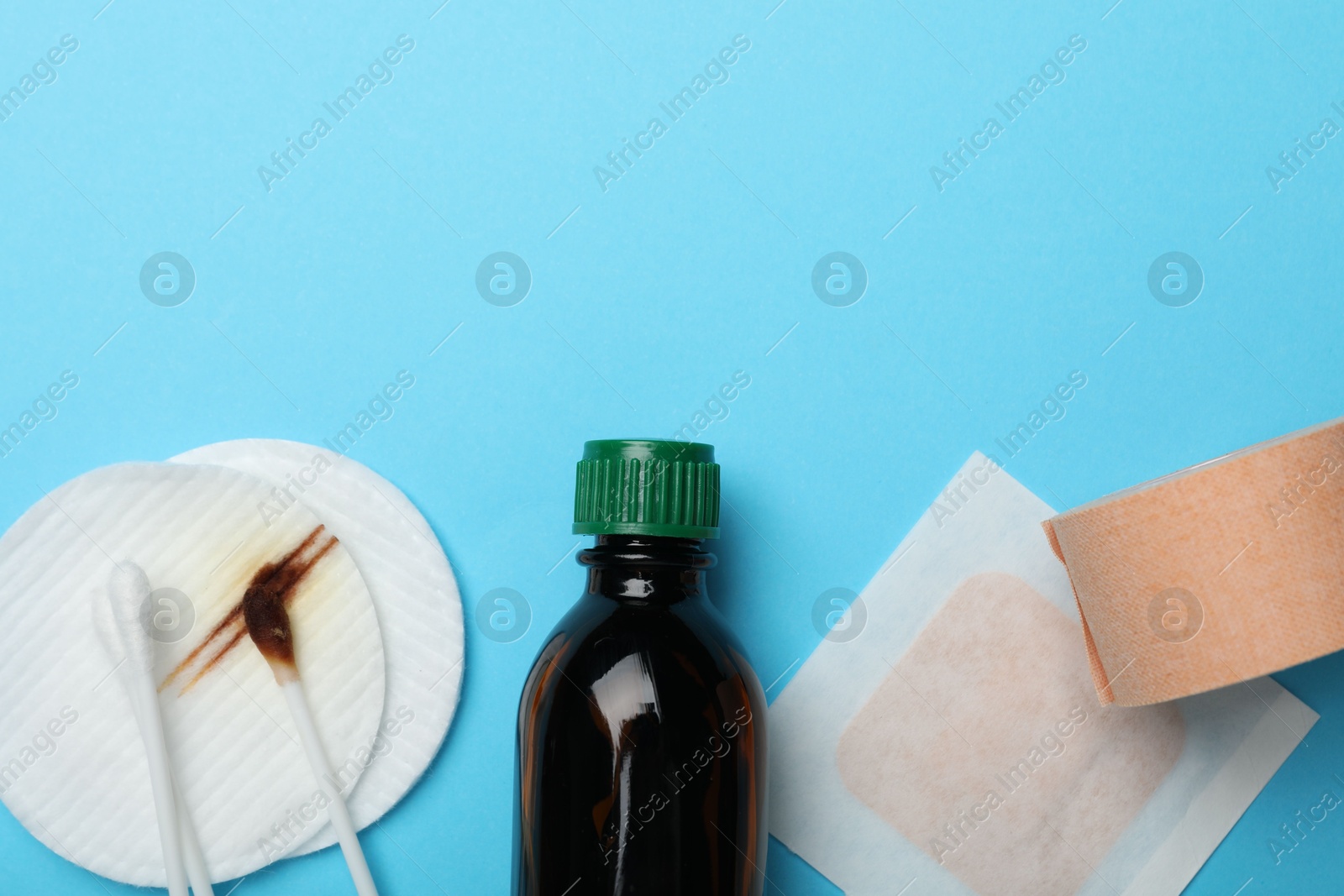 Photo of Topical iodine and other first aid kit components on light blue background, flat lay. Space for text