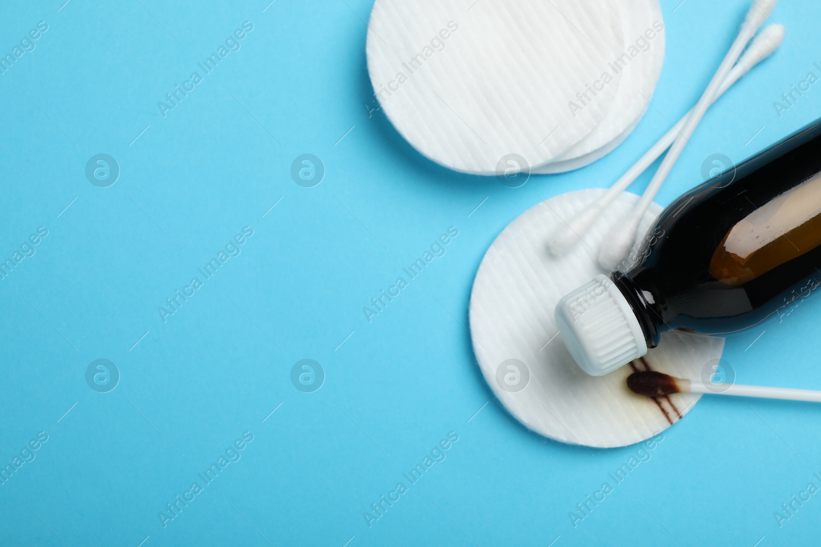 Photo of Topical iodine, cotton pads and swabs on light blue background, flat lay