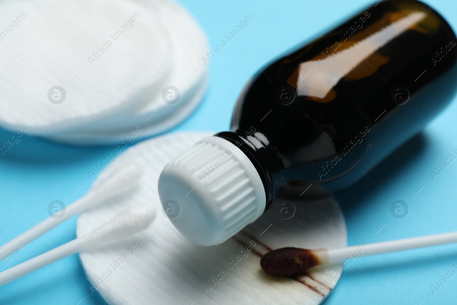 Photo of Bottle of topical iodine, cotton pads and swabs on light blue background, closeup