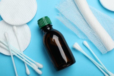 Topical iodine, bandage, cotton pads and swabs on light blue background, flat lay