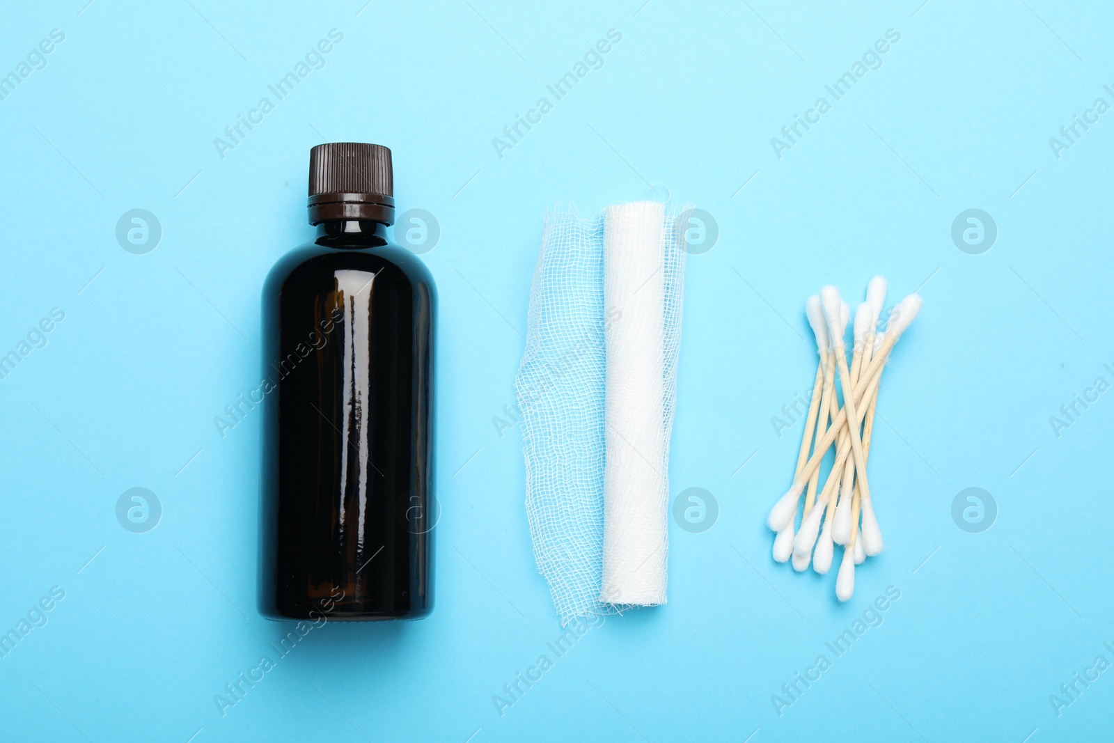 Photo of Topical iodine, bandage and cotton swabs on light blue background, flat lay