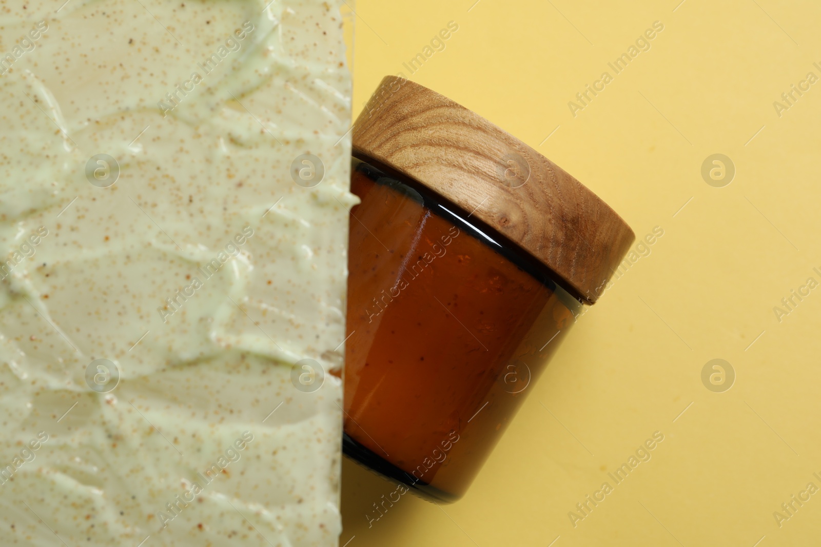 Photo of Cosmetic jar and sample of body scrub on yellow background, top view