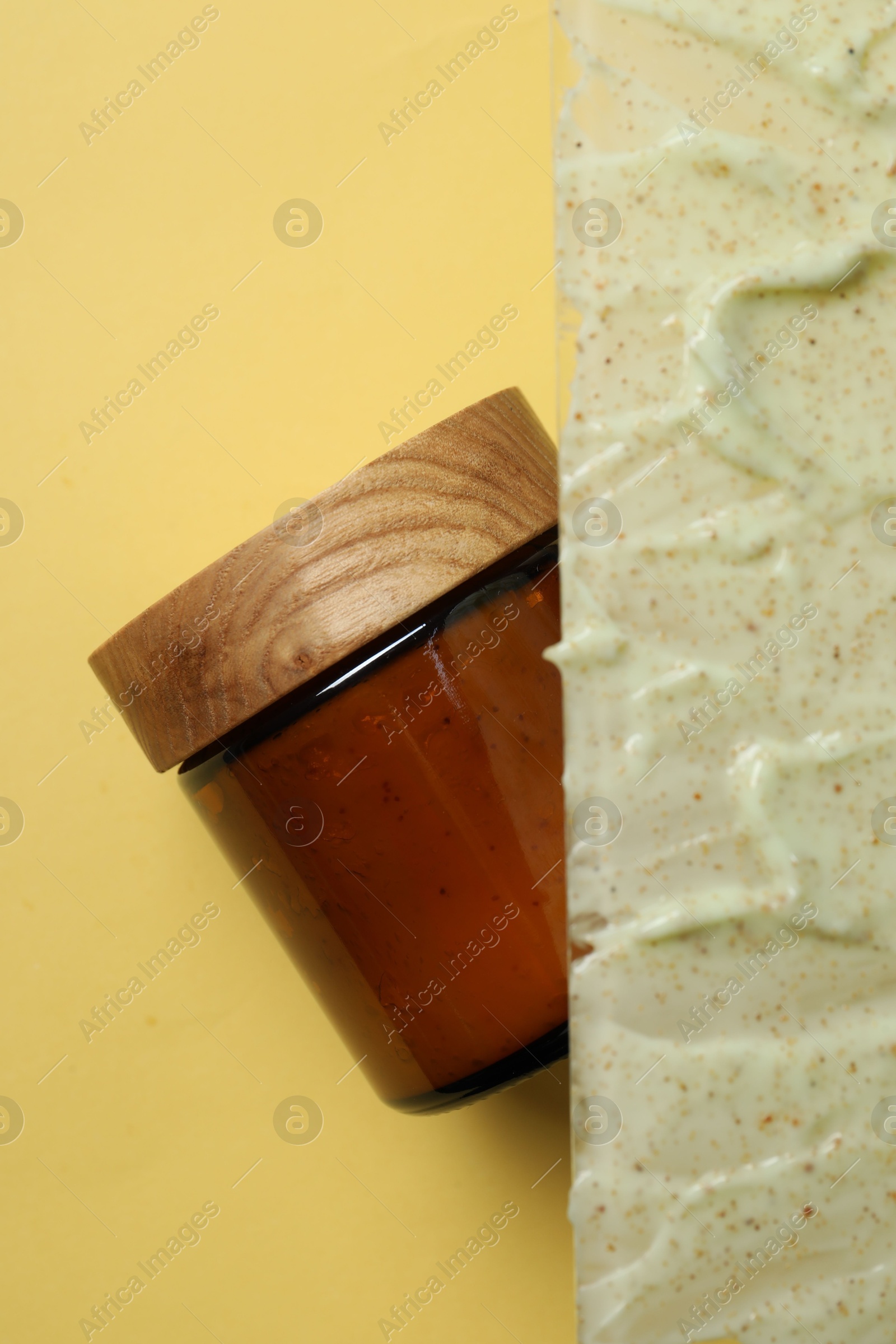 Photo of Cosmetic jar and sample of body scrub on yellow background, top view