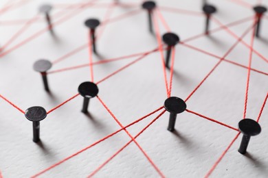 Photo of Network connection. Nails linked together by thread on white table, closeup