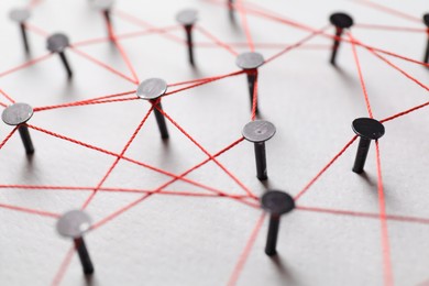 Photo of Network connection. Nails linked together by thread on white table, closeup