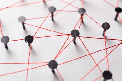 Network connection. Nails linked together by thread on white table, closeup