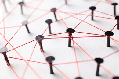 Network connection. Nails linked together by thread on white table, closeup