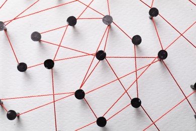 Photo of Network connection. Nails linked together by thread on white table, top view